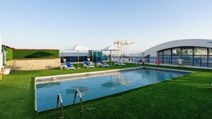 Una piscina con tumbonas y sombrillas, rodeada de césped cuidado.