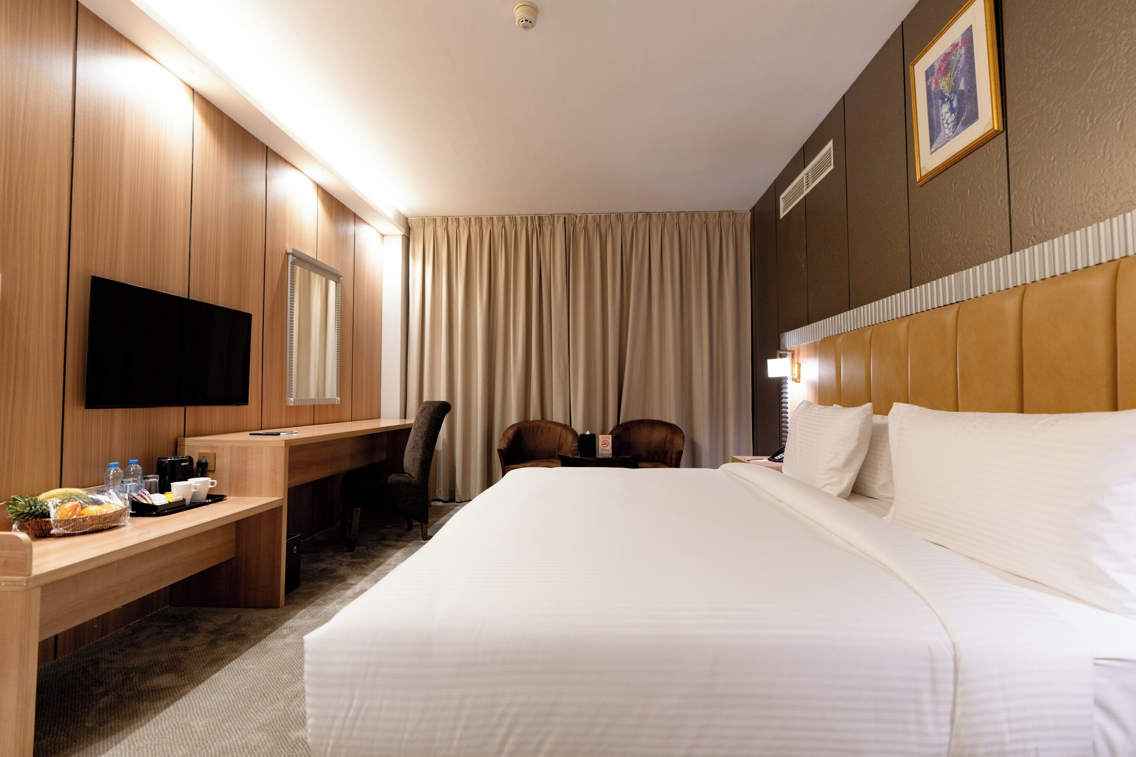 Une chambre d’hôtel avec un grand lit, un bureau avec une chaise, une télévision et une fenêtre avec des rideaux.
