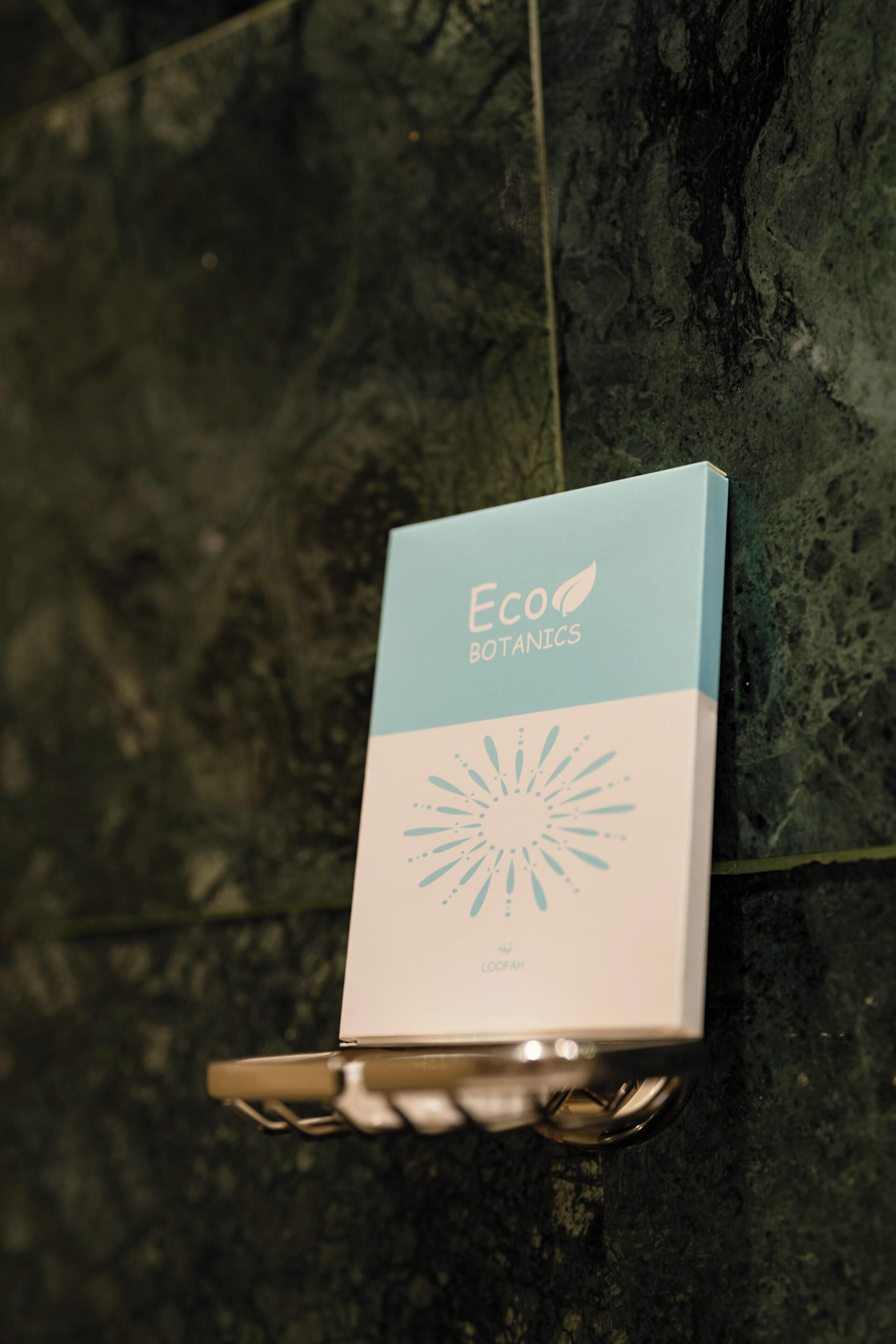 Une boîte étiquetée « Eco Botanics » est posée sur une étagère en métal, adossée à un mur sombre à la texture marquée.