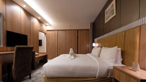 Una habitación de hotel con cama, escritorio, silla, televisor y mesita de noche.