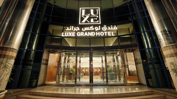 La entrada del HOTEL LUXE GRAND con fachada de vidrio y un letrero llamativo.