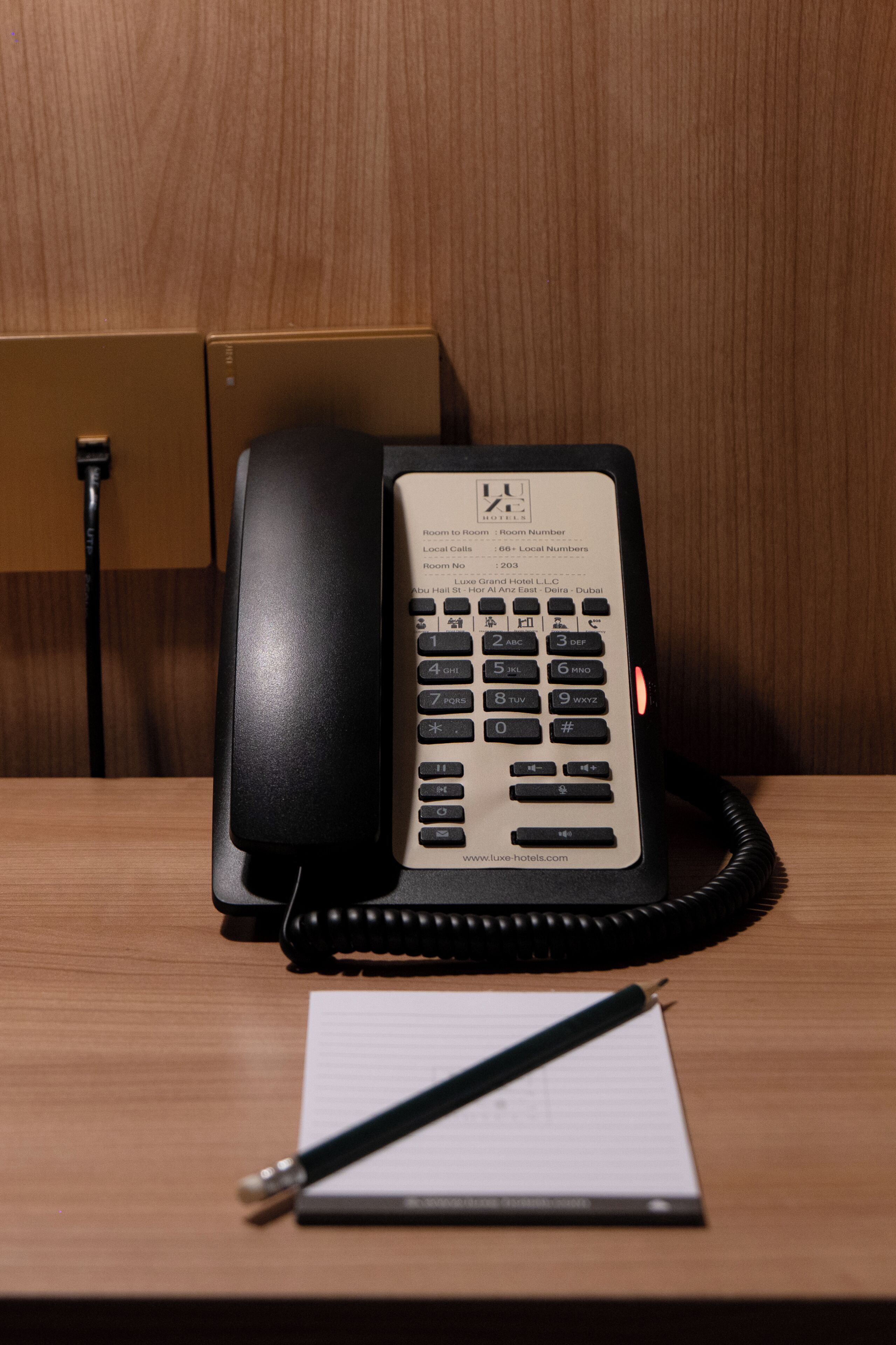 A hotel phone on a desk with a notepad and pen.