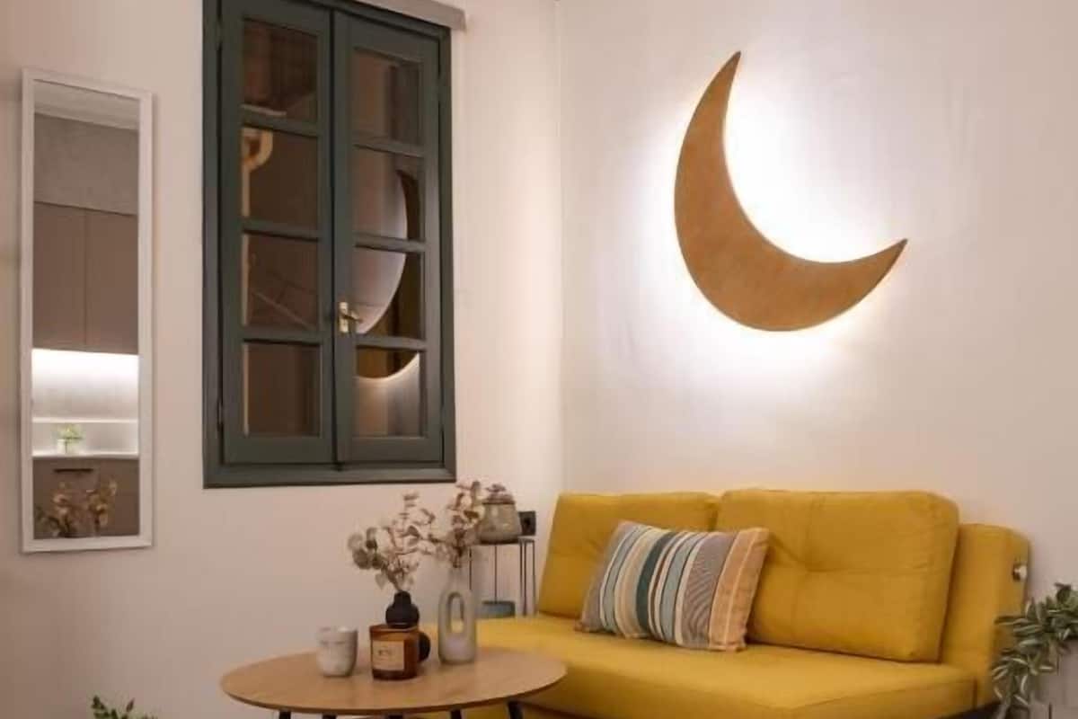 A cozy living room with a yellow sofa, a round coffee table, and a crescent moon wall decoration.