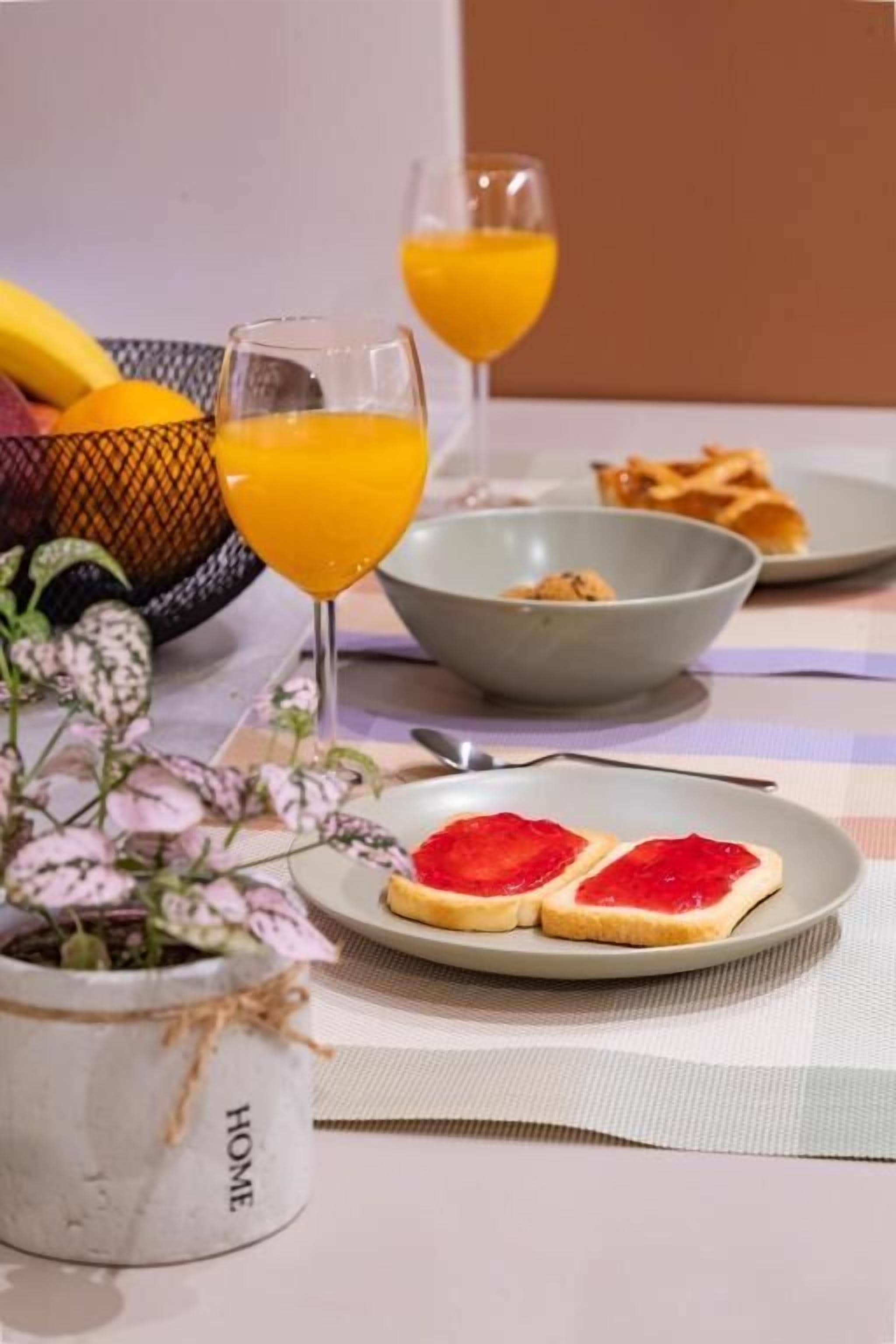 Een ontbijtsetting met een bord toast, een kom en twee glazen sinaasappelsap.