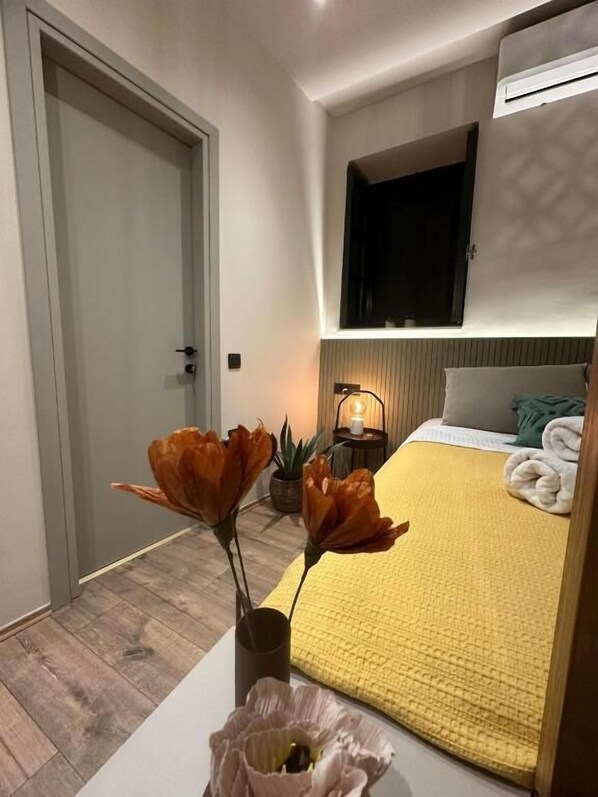 A bedroom with a bed, a bedside table with a vase of flowers, a nightstand with a lamp, and a wall-mounted TV. - La Luna Luxury Stay (Nafplio)