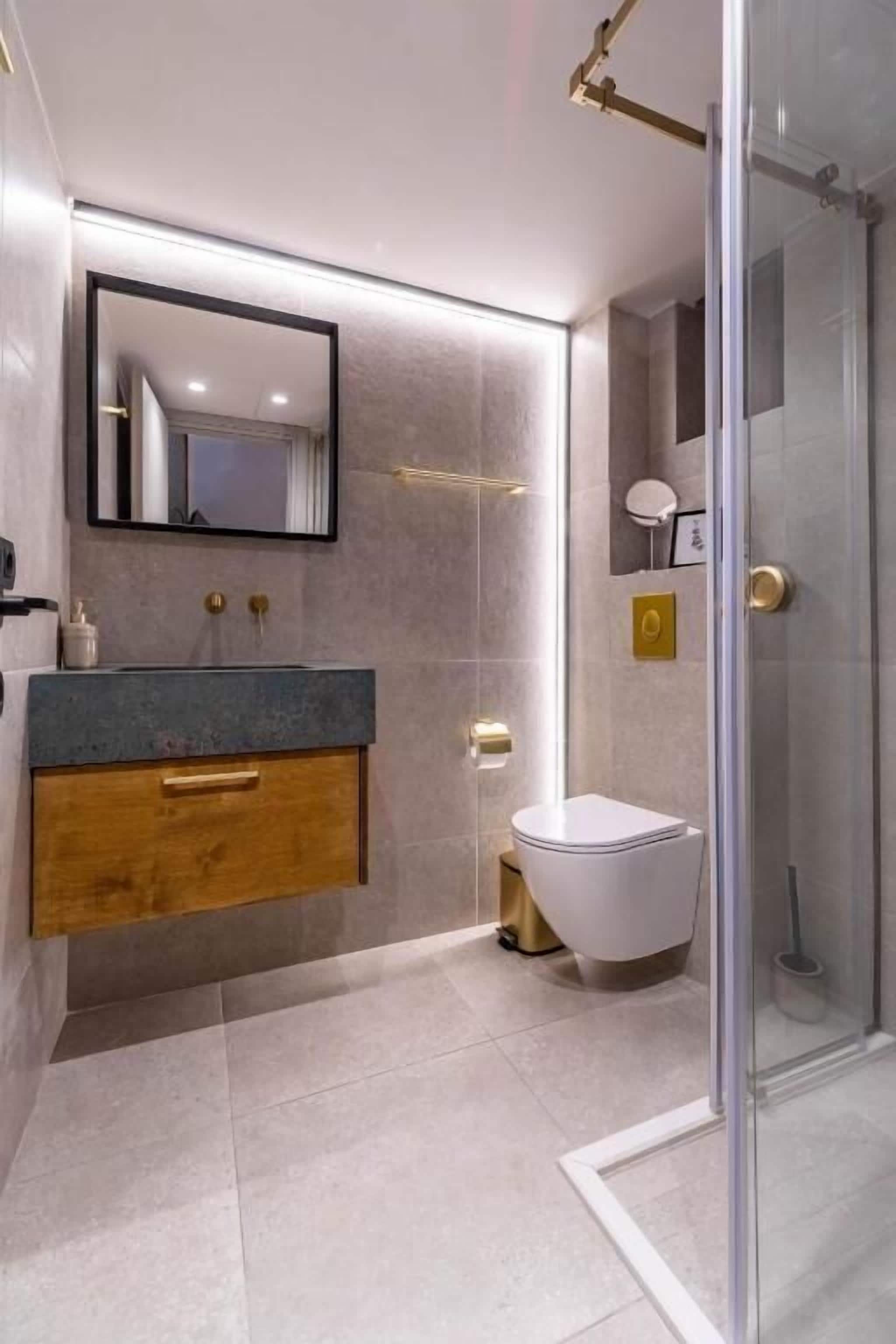 Une salle de bain moderne avec une douche à parois de verre, un meuble-lavabo en bois et des toilettes blanches.
