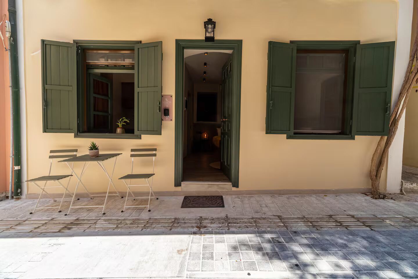 A building with a small outdoor seating area, a door leading to an interior space, and a staircase to the right.