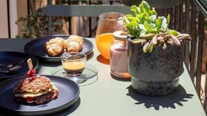 Et bord med kager, et glas juice og en potteplante på en balkon.