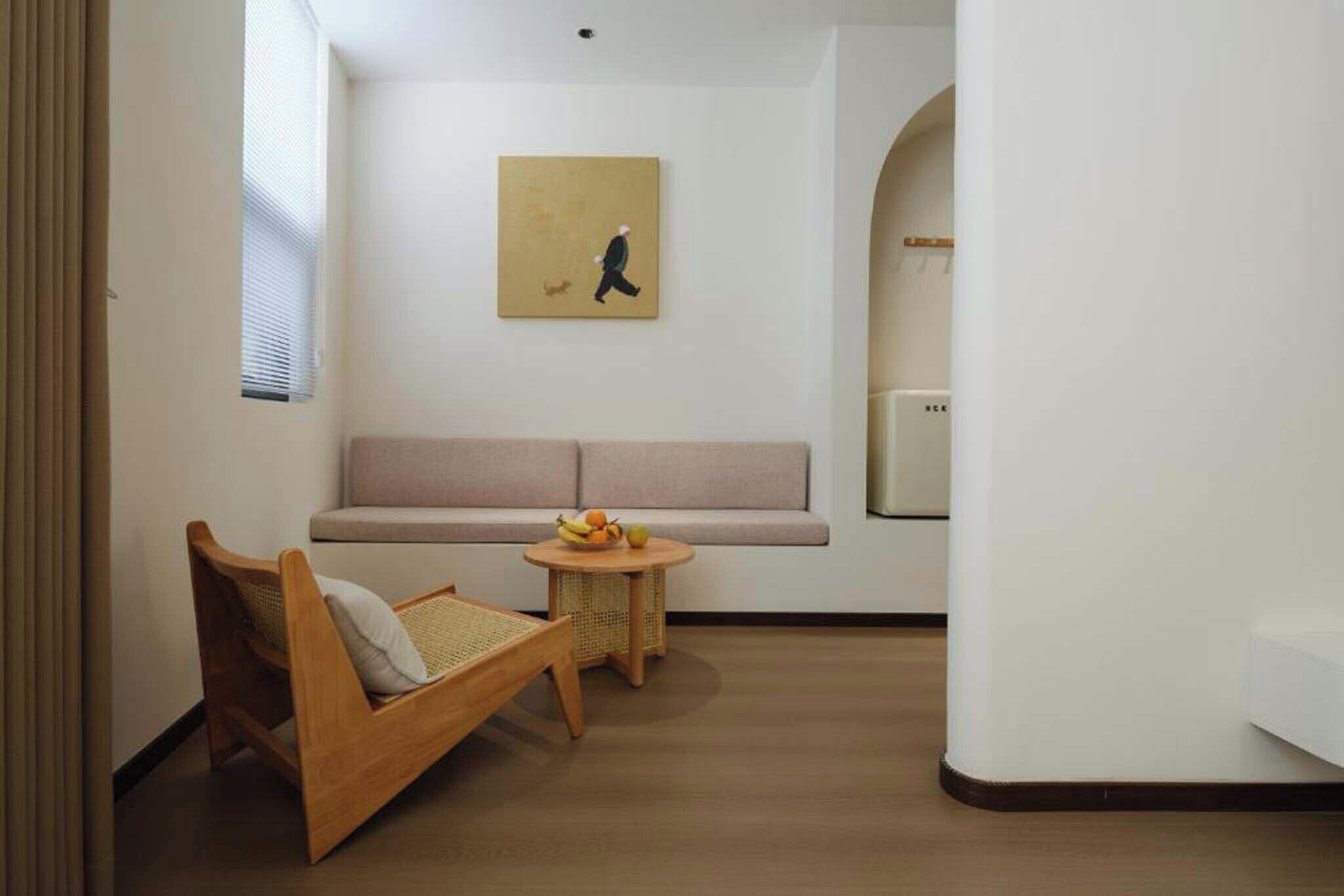 A modern living room with a sofa, a wooden chair, a small round table with fruit, and a painting on the wall.