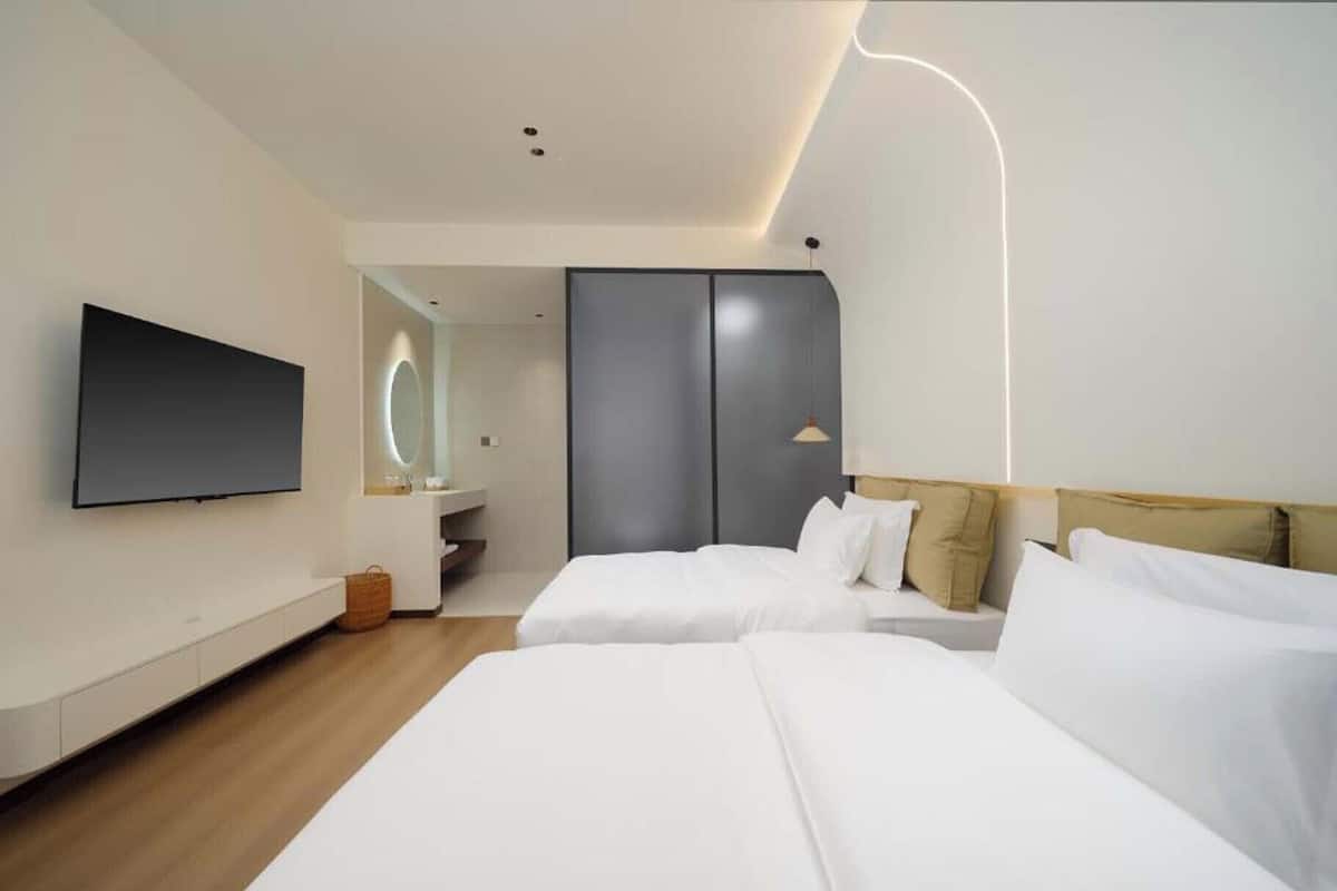 Ein modernes Hotelzimmer mit zwei Betten, einem Fernseher, einem Badezimmer und einem Kleiderschrank.