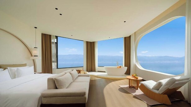 A modern hotel room with a large bed, a sofa, a bathtub, and a view of the sea. - Dali Fanxi Manhai Holiday Guesthouse (Dali)