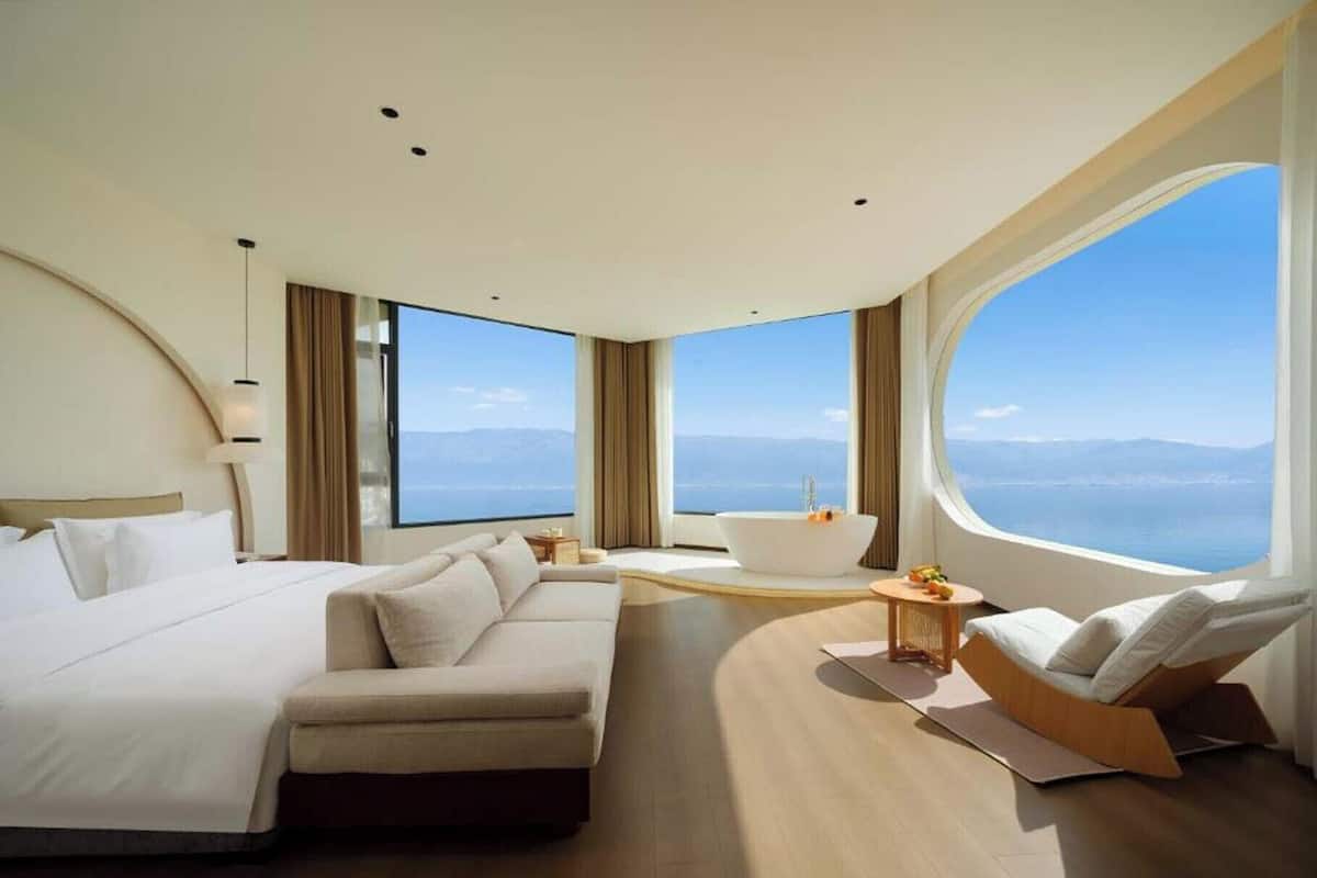 Ein modernes Hotelzimmer mit einem großen Bett, einer Couch, einer Badewanne und Meerblick.
