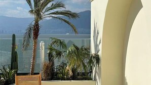 A balcony with a view of the sea, featuring a palm tree, a wooden bench, and a wicker table. - Dali Fanxi Manhai Holiday Guesthouse (Dali)