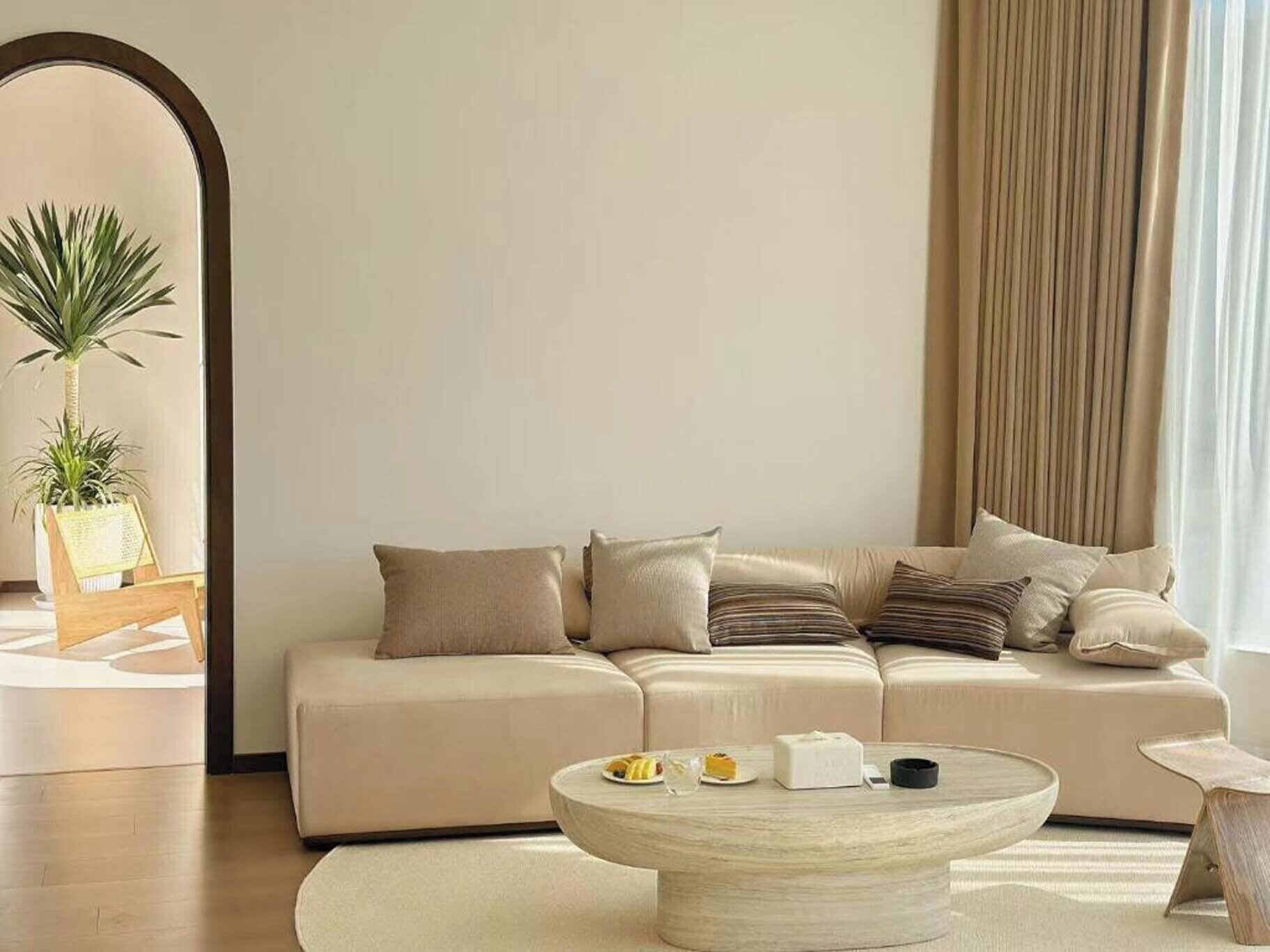 Una sala de estar moderna con un sofá color beige, una mesita de centro redonda y una planta en maceta.