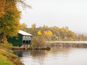 Una casa verde junto a un lago tranquilo, con una ladera boscosa al fondo.