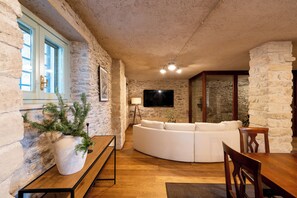 A cozy living room with a stone wall, a white sofa, a wooden table, and a TV mounted on the wall. - Luxury 7BR Villa | Private Pool & Lake Garda View | Limonaia dei Dogi | Gargnano (Gargnano)