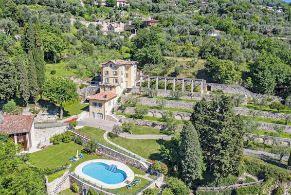 Oversigtsbillede af en villa med swimmingpool, omgivet af frodig vegetation og stendækkede stier.