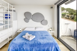 Une chambre à coucher avec un grand lit, une armoire, une table de chevet et une fenêtre donnant sur des arbres et des immeubles.