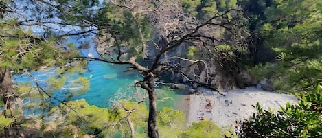 A coastal landscape with rocky cliffs, clear blue water, and a sandy beach.