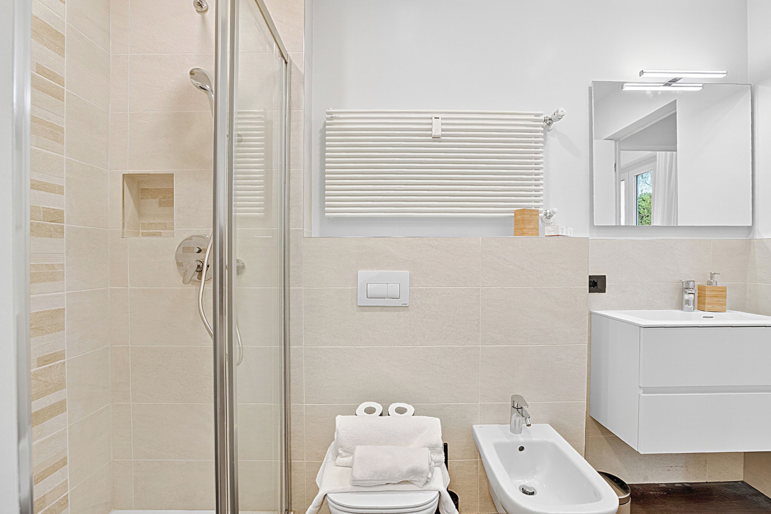 A modern bathroom with a glass shower enclosure, a bidet, and a white sink.