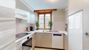 A compact kitchen with white cabinets, a built-in oven, a sink, and two potted plants. - Spacious 3-Bedroom Apartment with Balcony & Mountain Views in Champfèr (Champfèr)