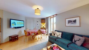 A living room with a TV, a dining table with chairs, a sofa, and a window with a view. - Spacious 3-Bedroom Apartment with Balcony & Mountain Views in Champfèr (Champfèr)