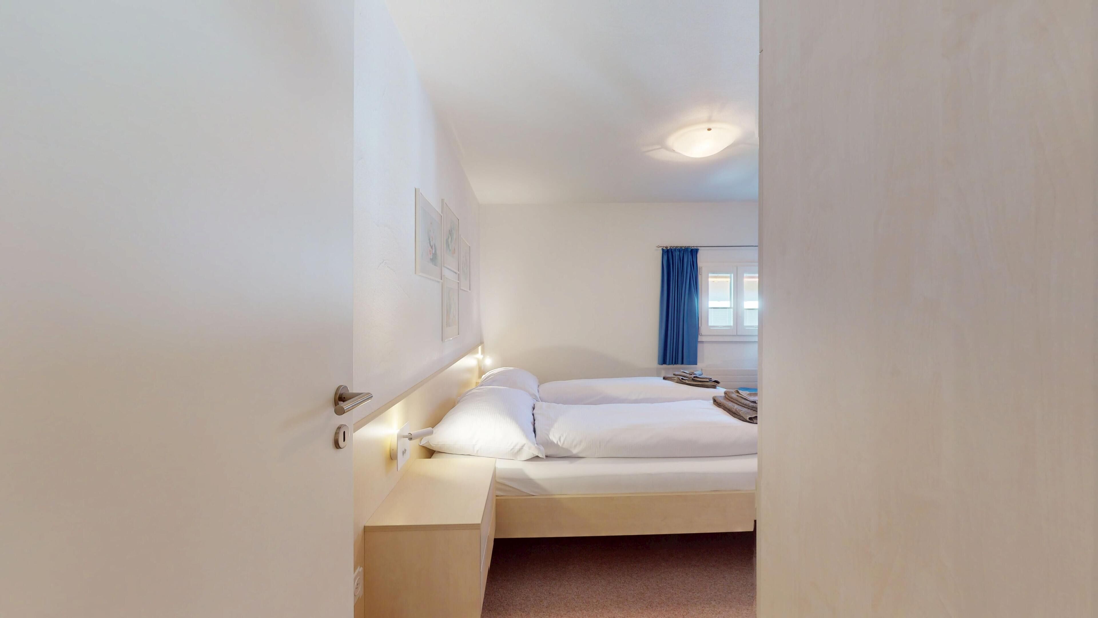 A bedroom with a bed, bedside tables, a window with curtains, and a ceiling light.