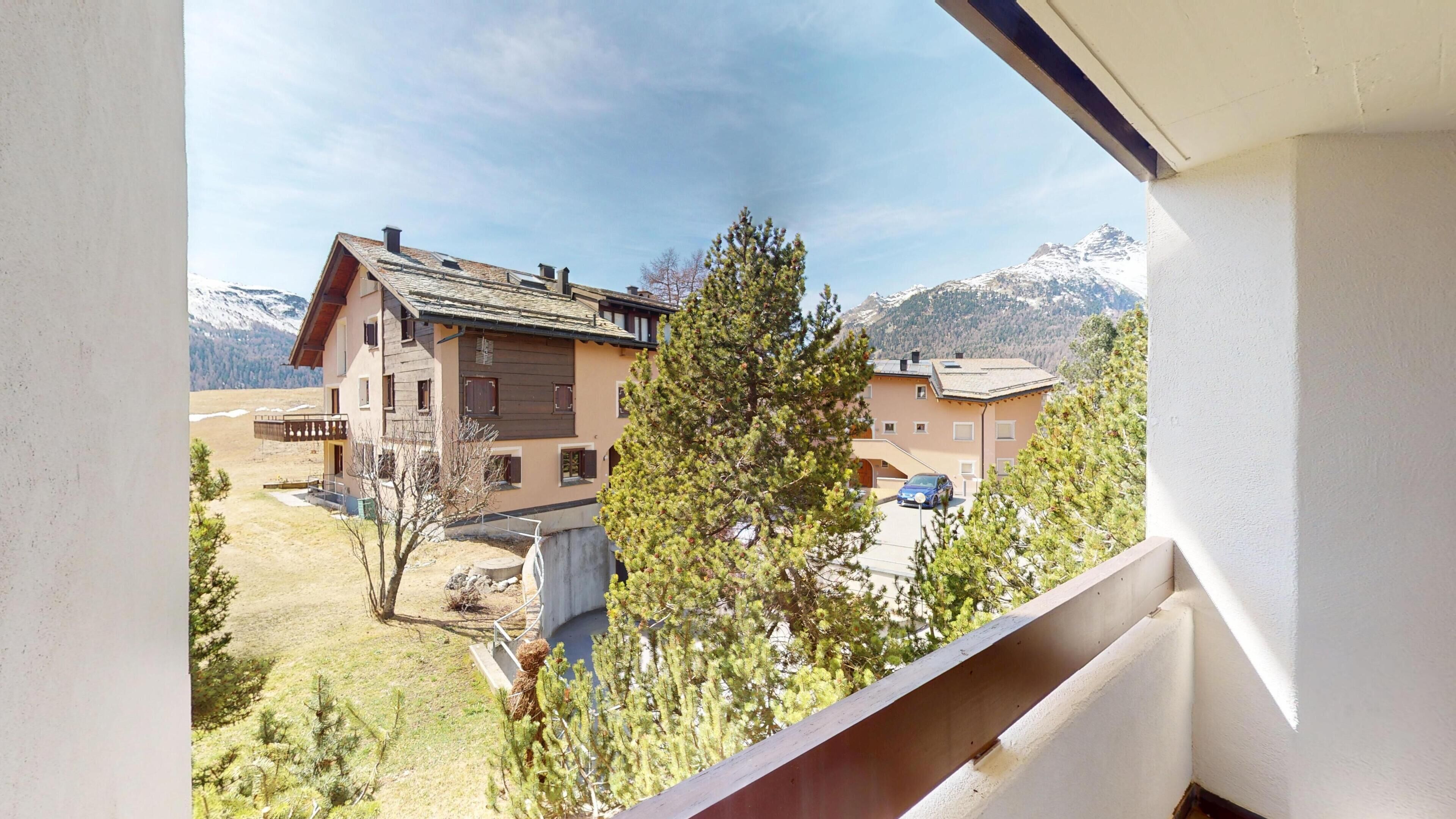 A mountain cabin with a sloped roof, a balcony, and a view of snow-capped mountains.