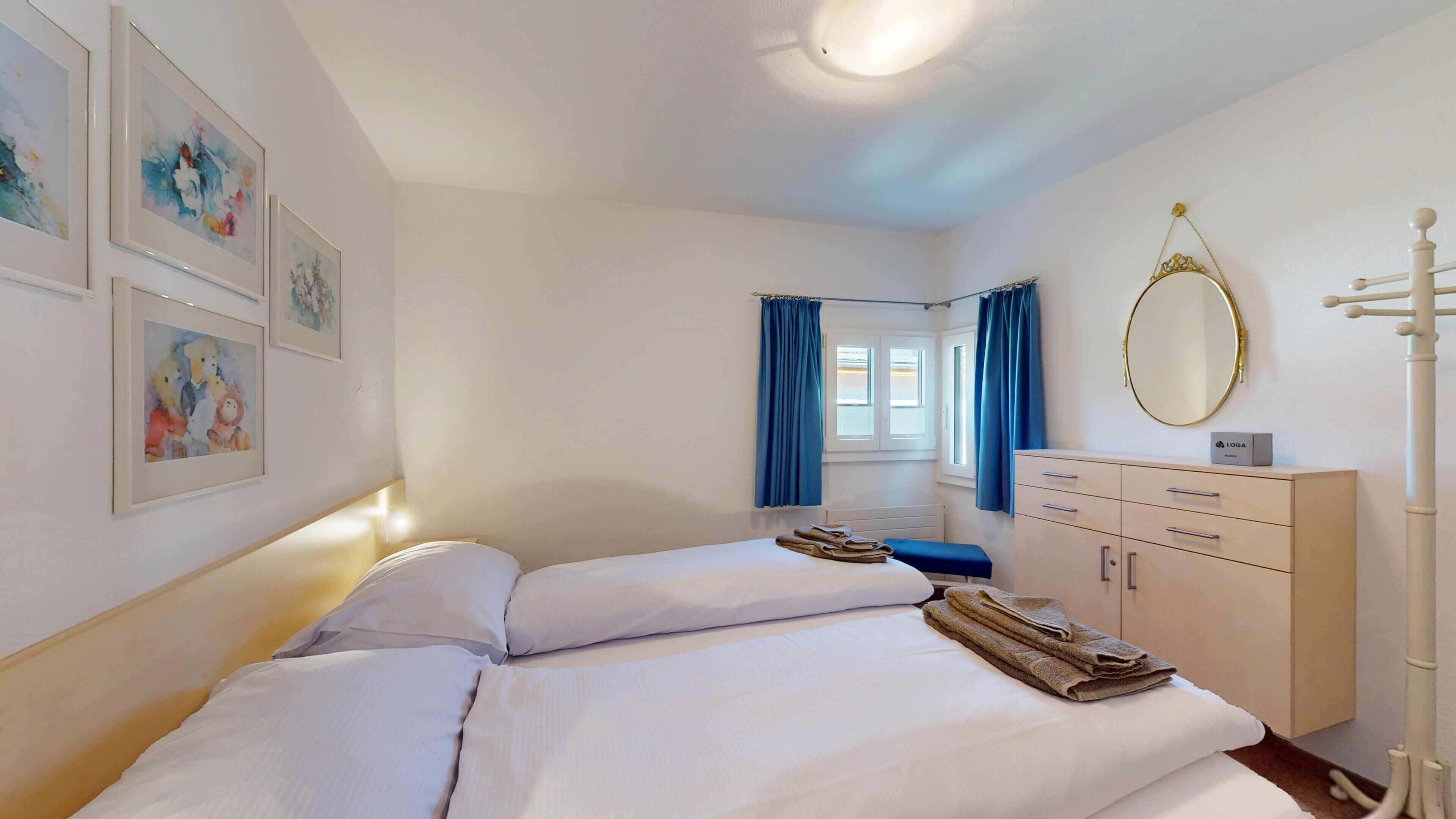 A bedroom with a bed, a dresser, a mirror, and artwork on the wall.