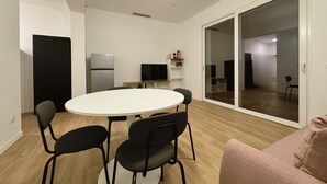 Une cuisine moderne équipée d’un réfrigérateur, d’un four à micro-ondes et d’un téléviseur à écran plat posé sur une étagère. On y trouve également une table de salle à manger ronde, accompagnée de quatre chaises.