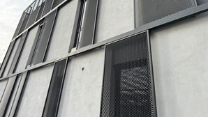 Une façade d’immeuble avec des fenêtres à treillis métallique vertical et un revêtement extérieur en béton.