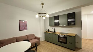 Une cuisine compacte au design moderne, dotée d’un îlot central, d’appareils électroménagers intégrés et d’un luminaire suspendu.
