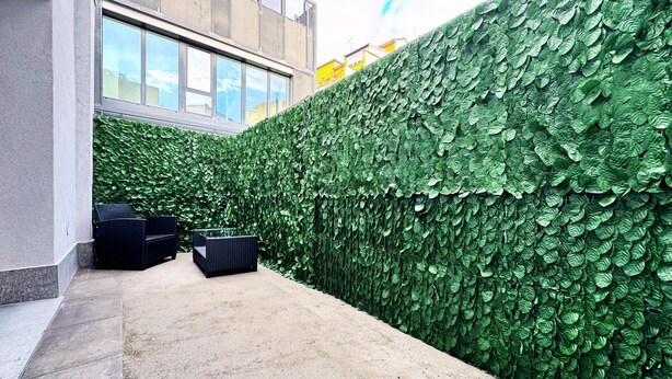 Un espace extérieur moderne agrémenté d’un mur végétal luxuriant, d’un chemin en béton et de mobilier en rotin noir.