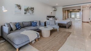 Una sala moderna con un sofá seccional gris, una mesita redonda y una pequeña mesa blanca. Hay dos cuadros enmarcados en la pared y una ventana al fondo.