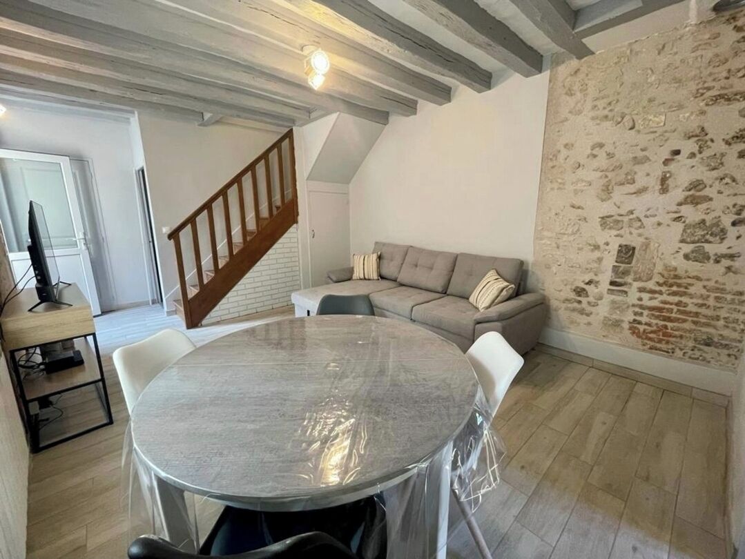 A cozy living room with a round table, a sofa, and a staircase.