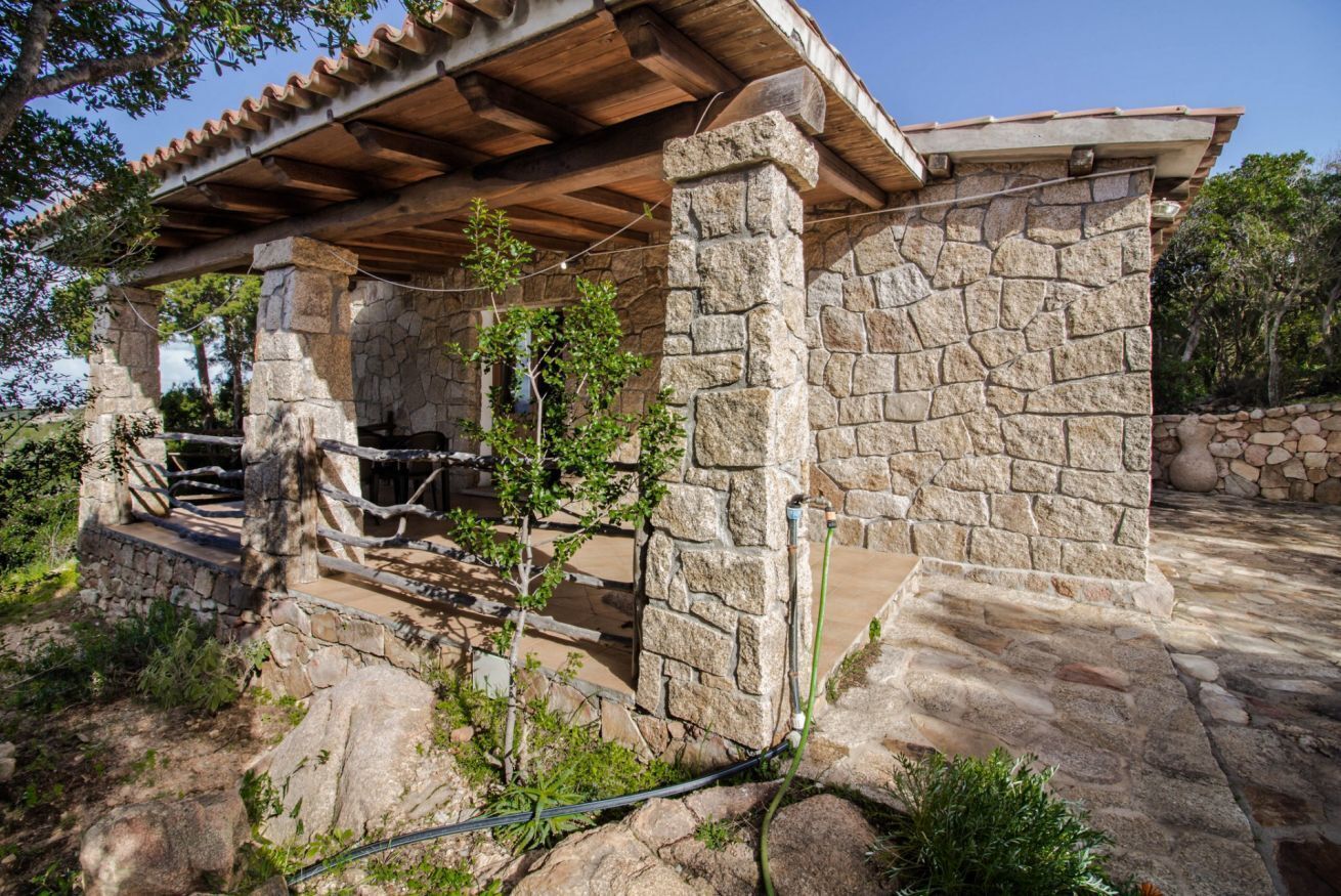 Un edificio in pietra con una pergola in legno, posti a sedere all'aperto e un muro di pietra.
