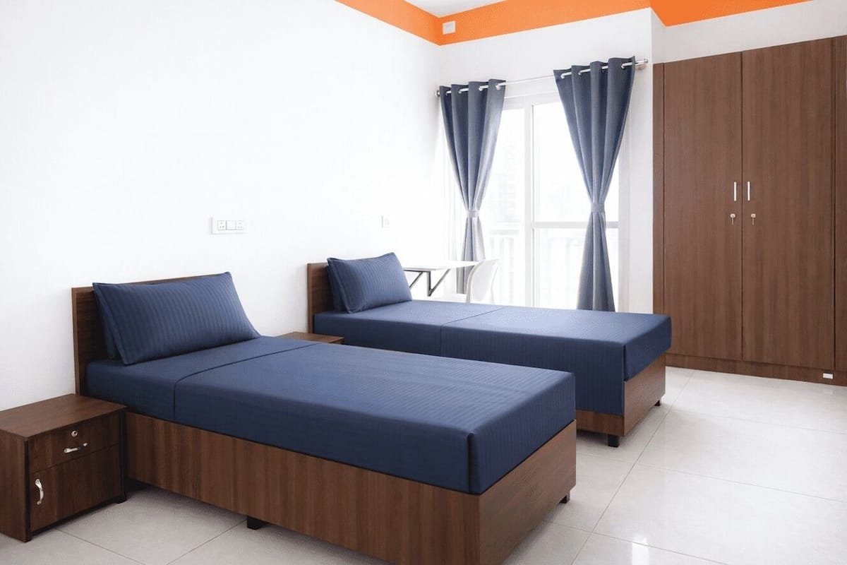 A bedroom with two beds, a wardrobe, and a window with curtains.