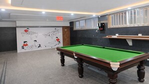 A billiards room with a pool table, a wall with illustrations of billiards, and a sign indicating the room is off. - Truliv Luna (Bengaluru)
