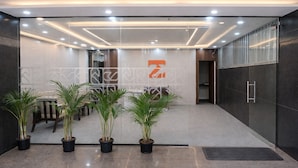 A modern reception area with a glass wall, potted plants, and a logo on the wall. - Truliv Luna (Bengaluru)