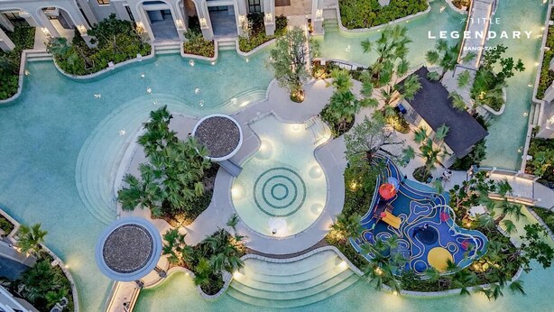 Vue aérienne d’un hôtel doté d’une piscine centrale, entouré de palmiers et d’un espace de jeux pour enfants.