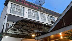 Un edificio de dos pisos con un letrero que dice "Homestay FLAMROYAN" y una antena parabólica en el techo.
