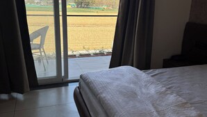 Une chambre d’hôtel avec un lit, une vue sur un champ par une porte coulissante et une chaise à l’extérieur.