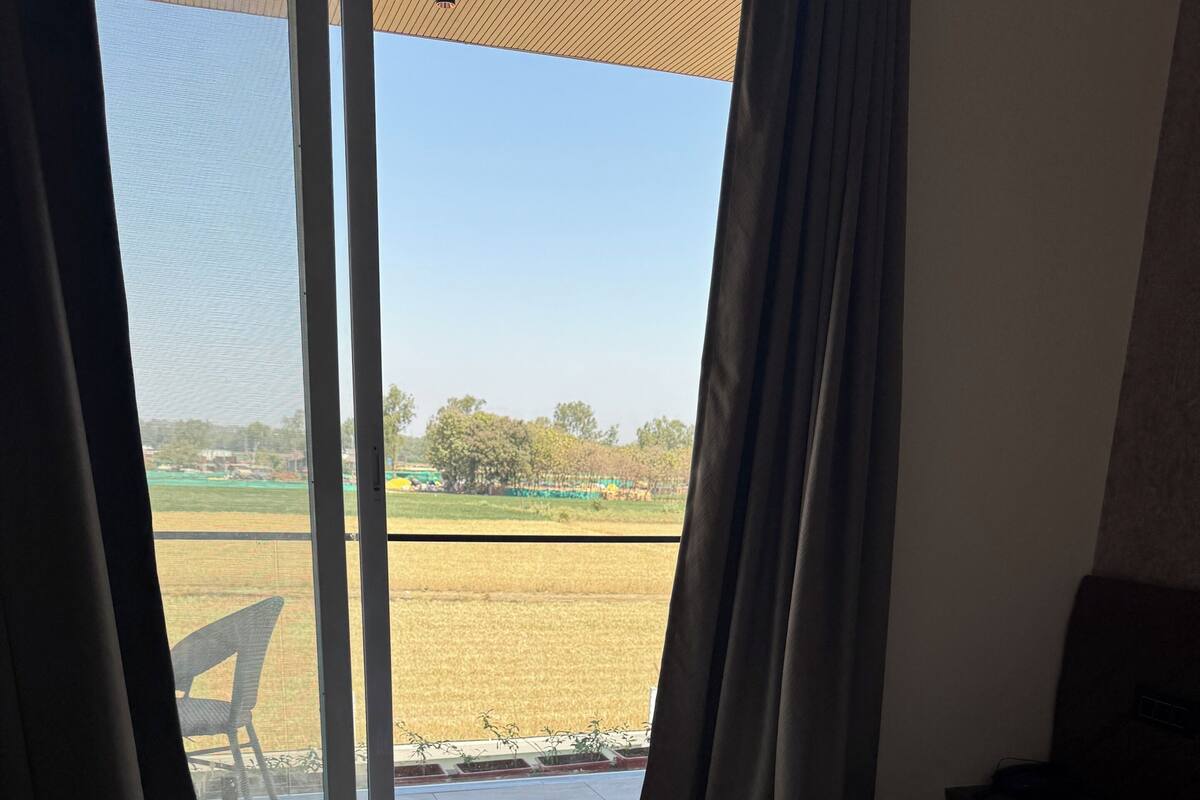 Une chambre d’hôtel avec un lit, une vue sur un champ par une porte coulissante et une chaise à l’extérieur.