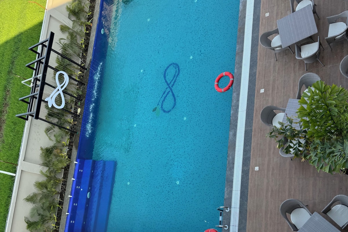 Vue aérienne d’une piscine avec une bouée de sauvetage, entourée de meubles de jardin et de verdure.