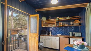 Cocina compacta con armarios de madera, microondas y tostadora. Un pequeño bote de basura y una libreta azul están sobre la encimera.