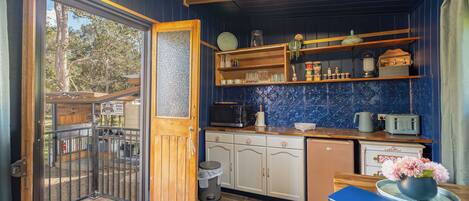 A compact kitchen with wooden cabinets, a microwave, and a toaster. A small trash bin and a blue notebook are on the counter.
