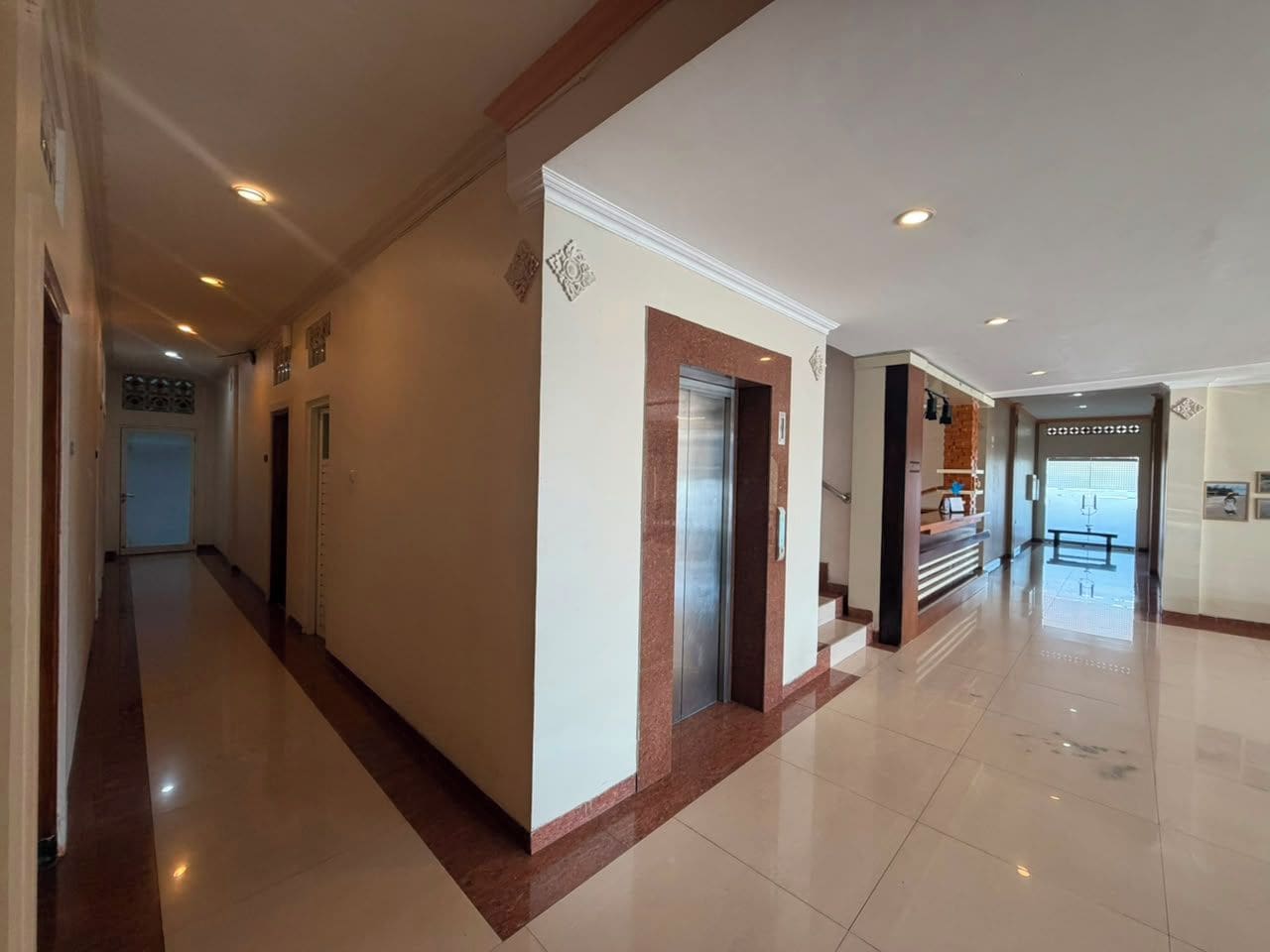 A hotel corridor with a reception desk, elevator, and a door at the end.