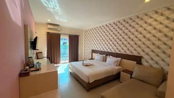A hotel room with a bed, a sofa, a desk with a kettle, and a television.