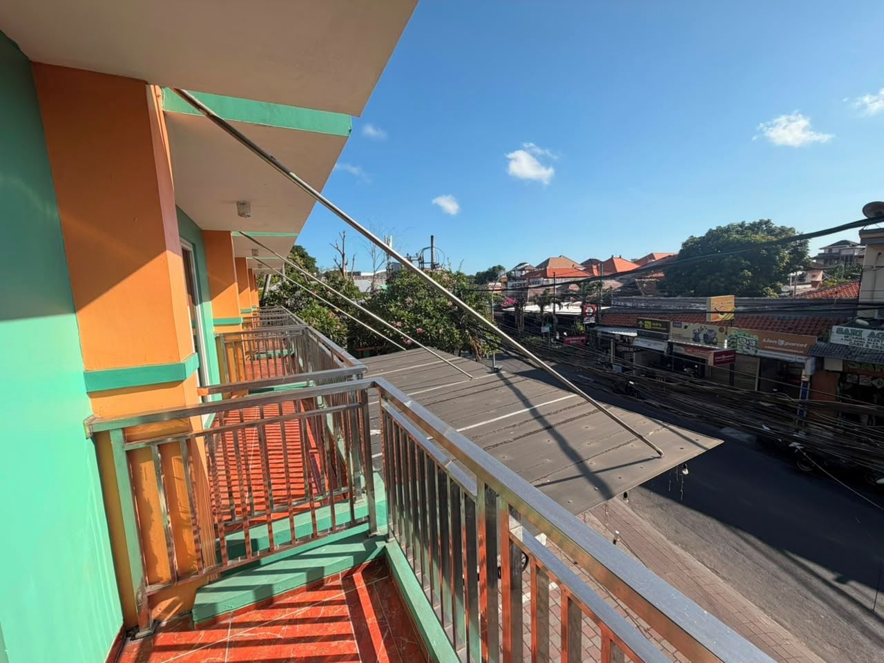 A balcony with a metal railing overlooking a street with buildings and a clear sky.