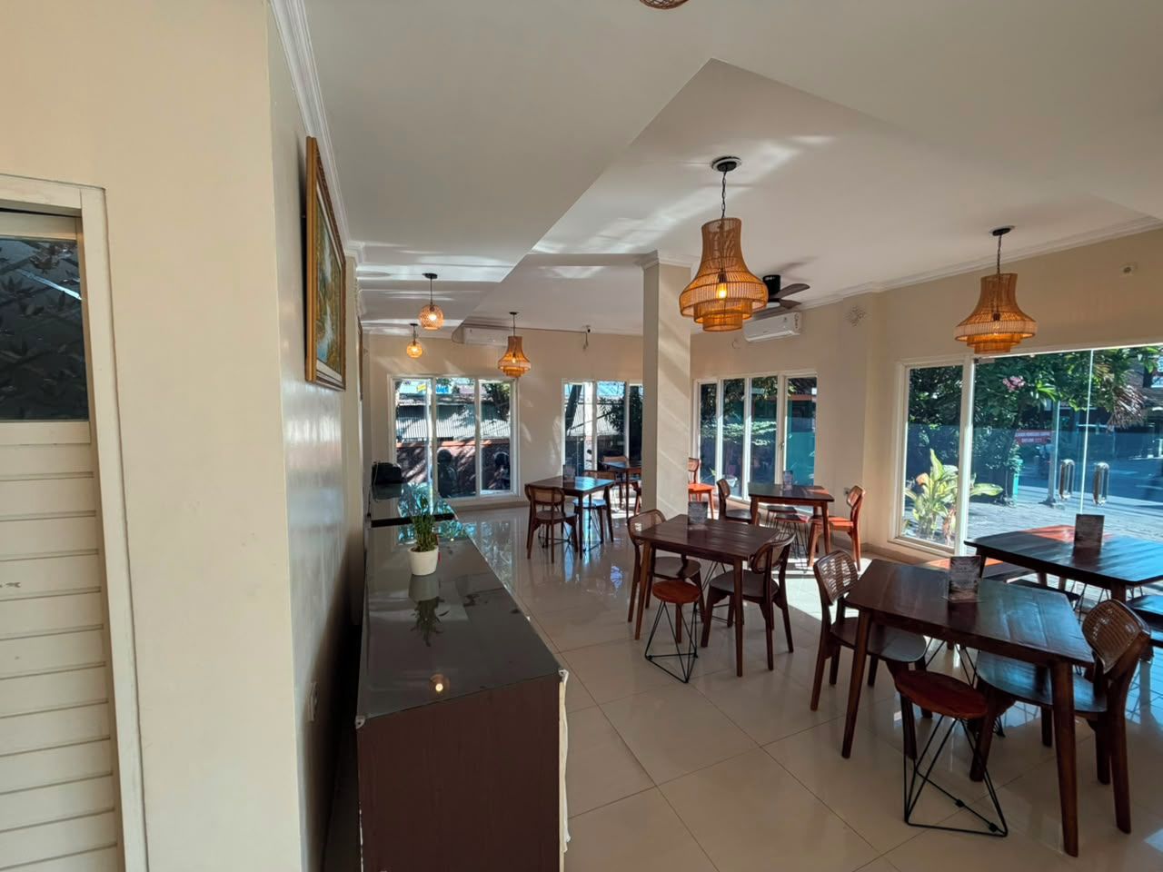 Un amplio comedor con varias mesas y sillas, ventanas grandes que ofrecen vistas al exterior, e iluminación colgante.